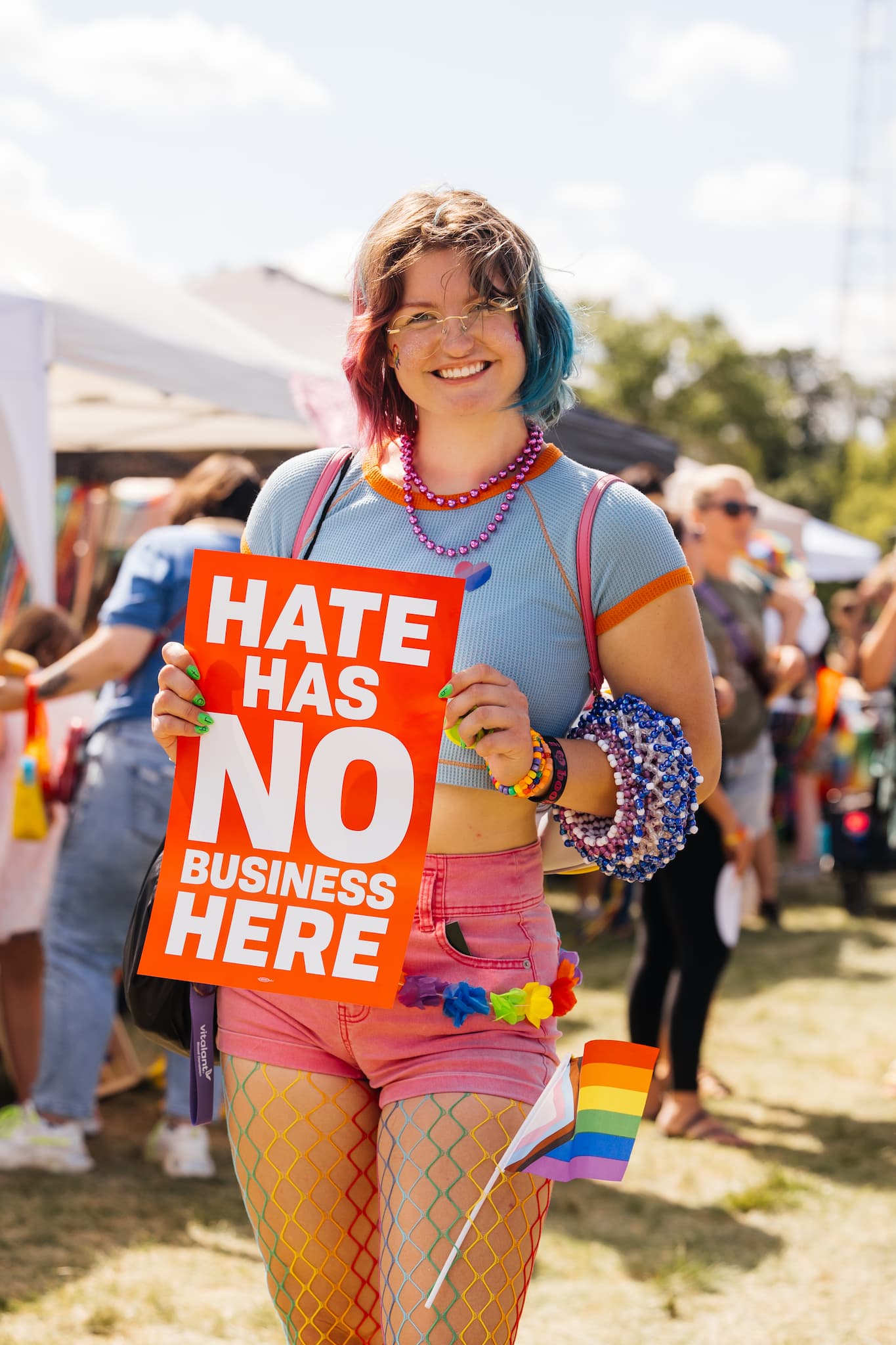 Woman at a pride event holds a colorful sign reading "Hate has no business here," promoting love and acceptance.