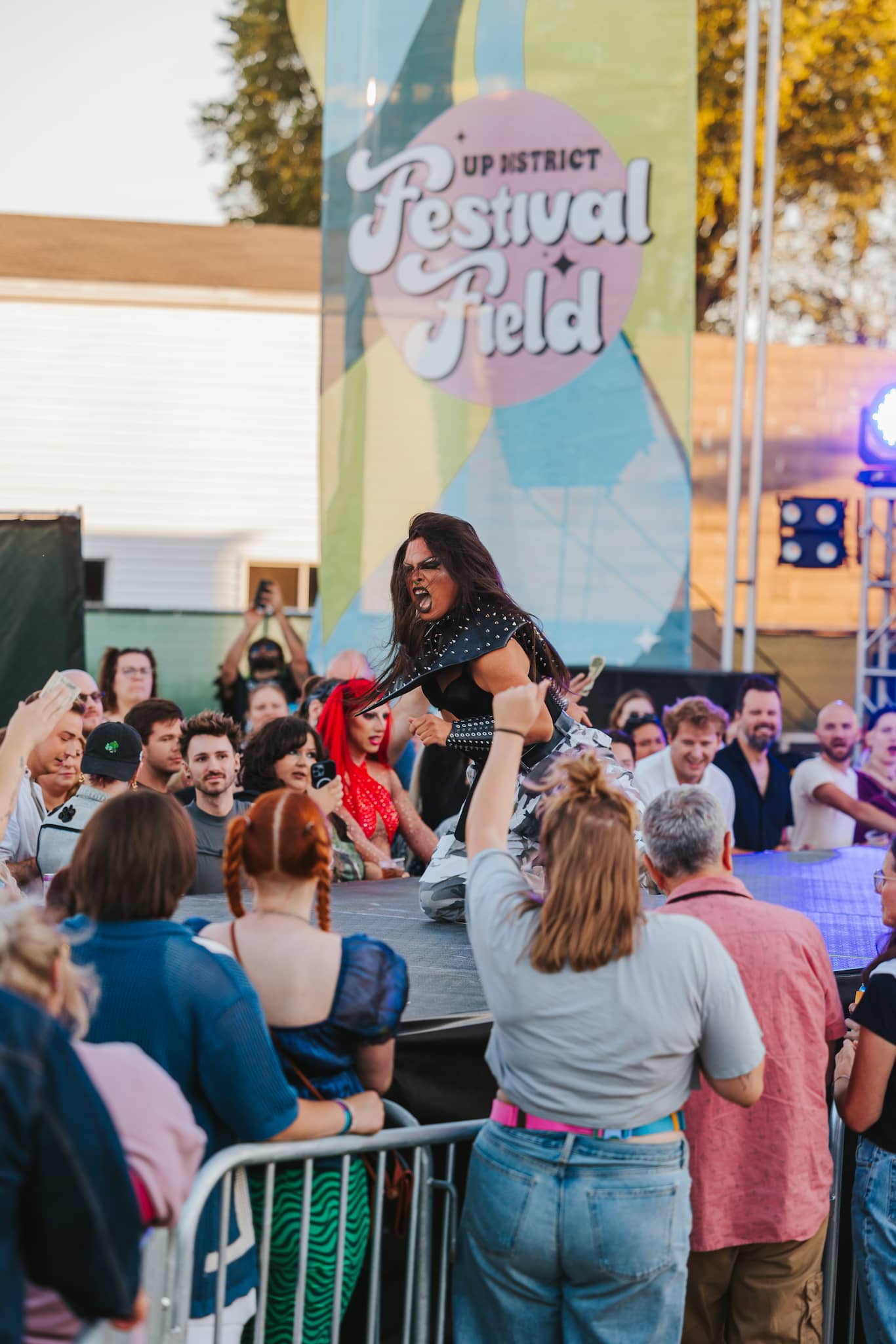 Colorful drag festival scene with a performer on stage, surrounded by an enthusiastic crowd celebrating pride.