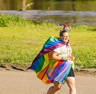 Woman runs joyfully in a rainbow cape, celebrating at a pride event, embodying the spirit of love and inclusivity.