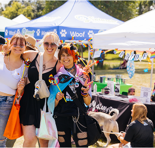 Three women stand together at a colorful pride event, celebrating diversity and LGBTQ+ pride