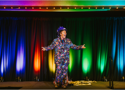 Performer with colorful dress on stage with vibrant lights, representing joy and support for the LGBTQ+ community.