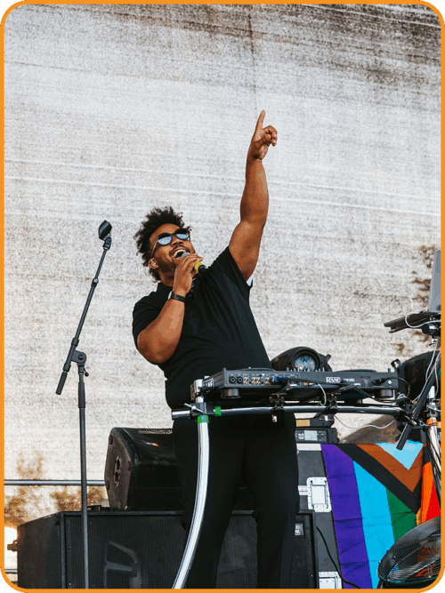 Man in sunglasses holds a microphone on stage at a colorful pride event for entertainment